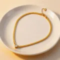 Detail view of the gold titanium steel heart zircon necklace displayed on a white plate. - White Zirconia Necklace