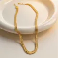 Closeup view of a gold herringbone chain necklace in a ceramic dish, elegant metal texture. - Necklace