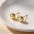 Detail shot of minimalist gold bezel pearl stud earrings in a white ceramic dish. - Stud Earrings