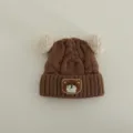 Detailed view of brown baby knitted hat with cute white pom-poms and lovely bear patch. - Suggested 1-3 Years (46-50cm) / Brown