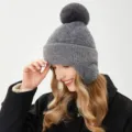 Nahaufnahme der grauen Strickmütze mit weichem Bommel und warmer Ohrenklappe Detailansicht. - M (54-58cm) / Grau