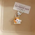 Detailed shot of the cute white puppy keychain pendant with yellow headphones and blue bow. - Westie Dog - Headphones