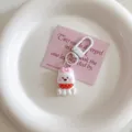 Close-up detail of a cute white puppy keychain with pink bow and red scarf inside a white dish. - Dog-Red Scarf