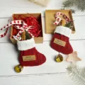 Dettaglio calza di Natale sospesa, calzino rosso in maglia con ramo di pino e campanella. - Pendaglio calza di Natale confezione regalo con biglietto d'auguri