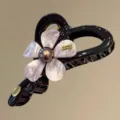 Detaillierte Nahaufnahme der eleganten schwarzen Haarklammer mit filigranem Harzblumen-Design. - Goldlabel-Buchstaben / Rosa