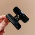 Primo piano dettagliato del elegante fermaglio per capelli nero a H con fiocco dorato. - Pinza Capelli Fiocco H / Nero