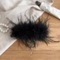 Detailed close-up of a black fluffy feather banana clip hair accessory on linen fabric. - Black Feather Banana Clip
