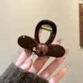 Primo piano dettagliato di un elegante mollettone marrone in resina con perla rotonda per acconciature. - Piccolo (8cm) / Cuore Perle Etichetta Oro Molla per Capelli