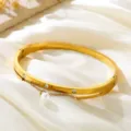 Pulsera rígida de acero inoxidable dorado con tres diamantes de imitación y dije de perla. - Dorado