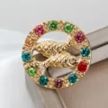 Dettaglio spilla rotonda dorata doppio pesce strass, gioiello di cristalli colorati brillanti. - Pesci (XZ25195)