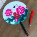 Ventilateur rond chinois traditionnel avec motif de pivoines, poignée noire et gland rouge. - Fleur de Papillon