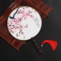 Eventail rond chinois traditionnel avec imprimé de prunier et pompon rouge. - Motif ruisseau au chant des oiseaux