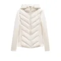 Close-up view of the beige hooded puffer jacket detail featuring chevron stitch and zipper. - XS / White