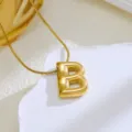 Gros plan détaillé d'un collier pendentif lettre B ballon doré sur support texturé blanc. - Or-Lettre B