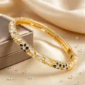 Bracelet jonc en métal doré avec émail floral blanc et noir et incrustation de strass brillants. - Blanc + Noir