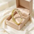 Primo piano di un bracciale rigido dorato con fiori in smalto rosa e strass in una scatola di raso. - Rosa