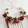 Primo piano dettagliato di una corona de fiori artificiale rosso scuro con bianche foglie. - Rosso