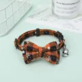 Detailed view of an orange and black plaid pet collar with a decorative bow and bell. - Orange Snowflake