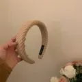 Detailopname van de brede beige gebreide haarbandtextuur met zachte stof en handgemaakt label. - Melkthee Kleur