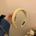 Gedetailleerd overzicht van een stijlvolle gele brede gebreide haarband met handgemaakt label. - Melkgeel