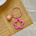 Detailansicht eines rosa Acryl-Stern-Schlüsselanhängers mit Glocke auf Zeitung - Rosa Stern Schlüsselanhänger