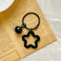 Detailed view of the black star-shaped acrylic pendant with a matching black bell. - Black Star Keychain