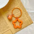 Detail of orange star-shaped acrylic keychain with small bell on newspaper background - Orange Star Keychain