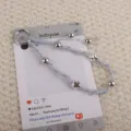 Handgemaakte gevlochten sleutelhanger met grijs waxkoord, metalen kralen en sterbedels. - Grijs