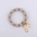 Detalle en primer plano del llavero pulsera de cuentas de silicona con anillas doradas. - Caqui