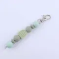 Silicone bead keychain detail shot featuring green round beads, rainbow charm, and metal clasp. - Bean Green