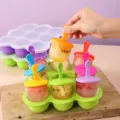 Nahaufnahme einer Hand, die ein Eis aus einer bunten 7-Loch-Silikonform für Kinder nimmt - 9-Loch Grün + Eisstiel