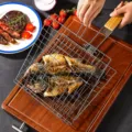 Detail view of stainless steel BBQ grilling basket holding grilled fish on wooden board - Standard Type