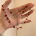 Detailed close-up of a delicate red beaded flower necklace, sweet choker jewelry item. - Red Weave
