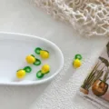 Close-up detail of handmade yellow and green glass fruit charm beads displayed in a white dish. - Lemon with Leaf