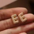 Detail shot of elegant gold letter E stud earrings, micro-paved with sparkling zircon stones. - Letter E