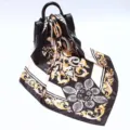 Detailed view of 90cm black and gold baroque floral print silk scarf draped on handbag. - D9190-Black