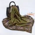 Detailed view of a green silk-feel square scarf with leopard chain print draped on black bag. - D9189-Army Green