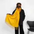 Close-up detail shot of a bright yellow imitation cashmere scarf with stylish fringe tassels. - Yellow