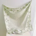 Close-up detail view of the green floral print square scarf draped elegantly on the table. - Green
