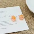 Detaillierte Nahaufnahme filigraner Blumen-Ohrstecker auf strukturierter weißer Karte. - Hellgelb Rosa
