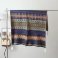 Detailed shot of the bohemian knitted blanket hanging on a metal rack with decorative tassels. - Sahara Dream Weaving / Brown