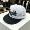 Vista detallada de gorra plana hip-hop en blanco y negro con bordado frontal y lateral. - Ajustable / Blanco [visera plana OUTLAW]