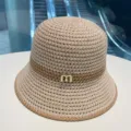 Beige straw bucket hat with contrast brown stripe and metal letter detail for summer sun protection. - Beige