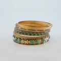 Close-up detail of stacked gold metal bangles featuring intricate floral textures and turquoise stones. - Gold