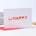 Tarjeta de felicitación calada con sonrisa naranja y sobre rojo para fiestas y cumpleaños. - HAPPY