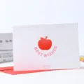 Tarjeta de felicitación blanca con sobre rojo, icono de manzana y texto para regalo festivo. - Mejores Deseos