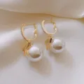 Exquisites Detail der goldenen Creolen mit Schleife, funkelnden Kristallen und Perle. - Weiße Perle