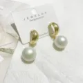 Detailansicht goldener, strukturierter C-förmiger Ohrringe mit eleganten weißen Perlen. - C-förmige weiße künstliche Perle