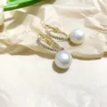 Detail view of C-shaped pearl hoop earrings with shiny rhinestones and a dangling white pearl charm. - Rhinestone-Set White Pearls