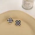 Detailed shot of black and white checkerboard square earrings with golden twisted metal edge. - Square Checkerboard Color-Preserving Gold
